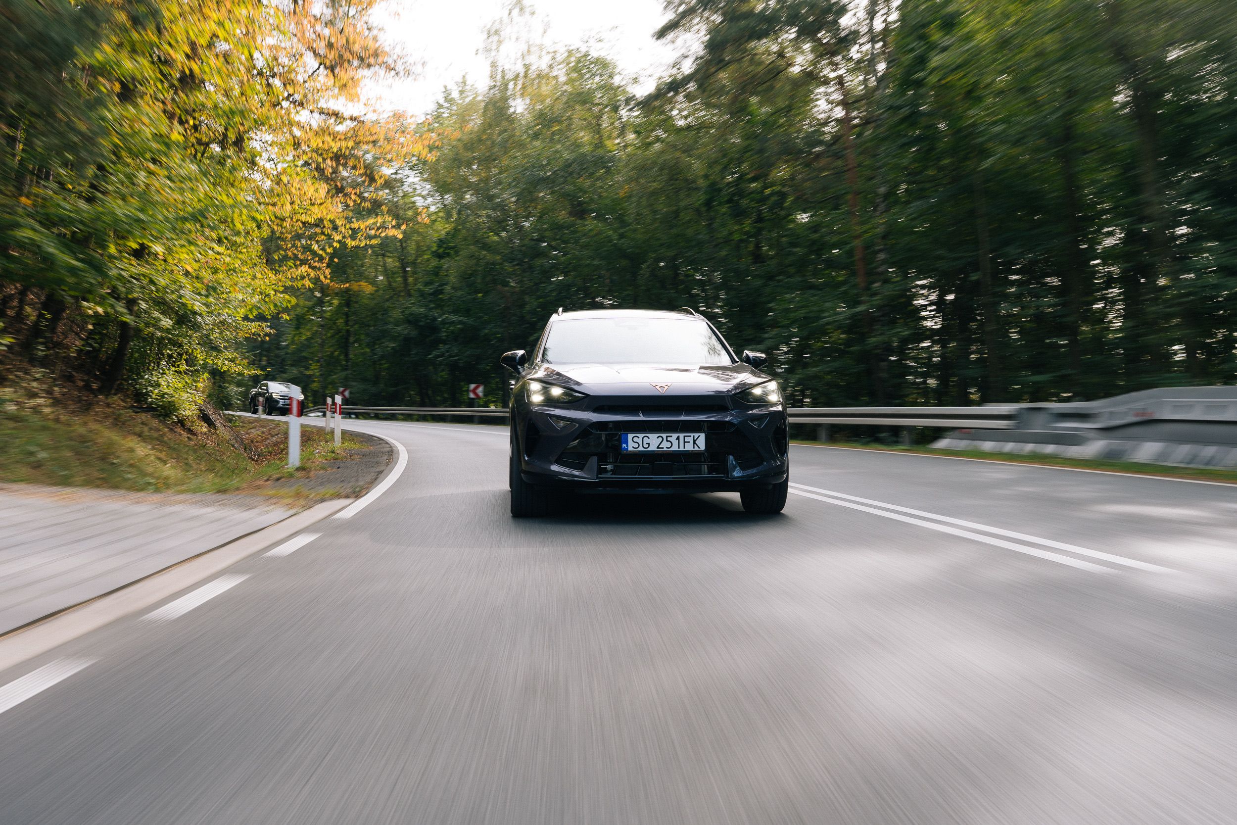 Ciemna CUPRA SUV nadjeżdża z naprzeciwka na zakręcie leśnej drogi