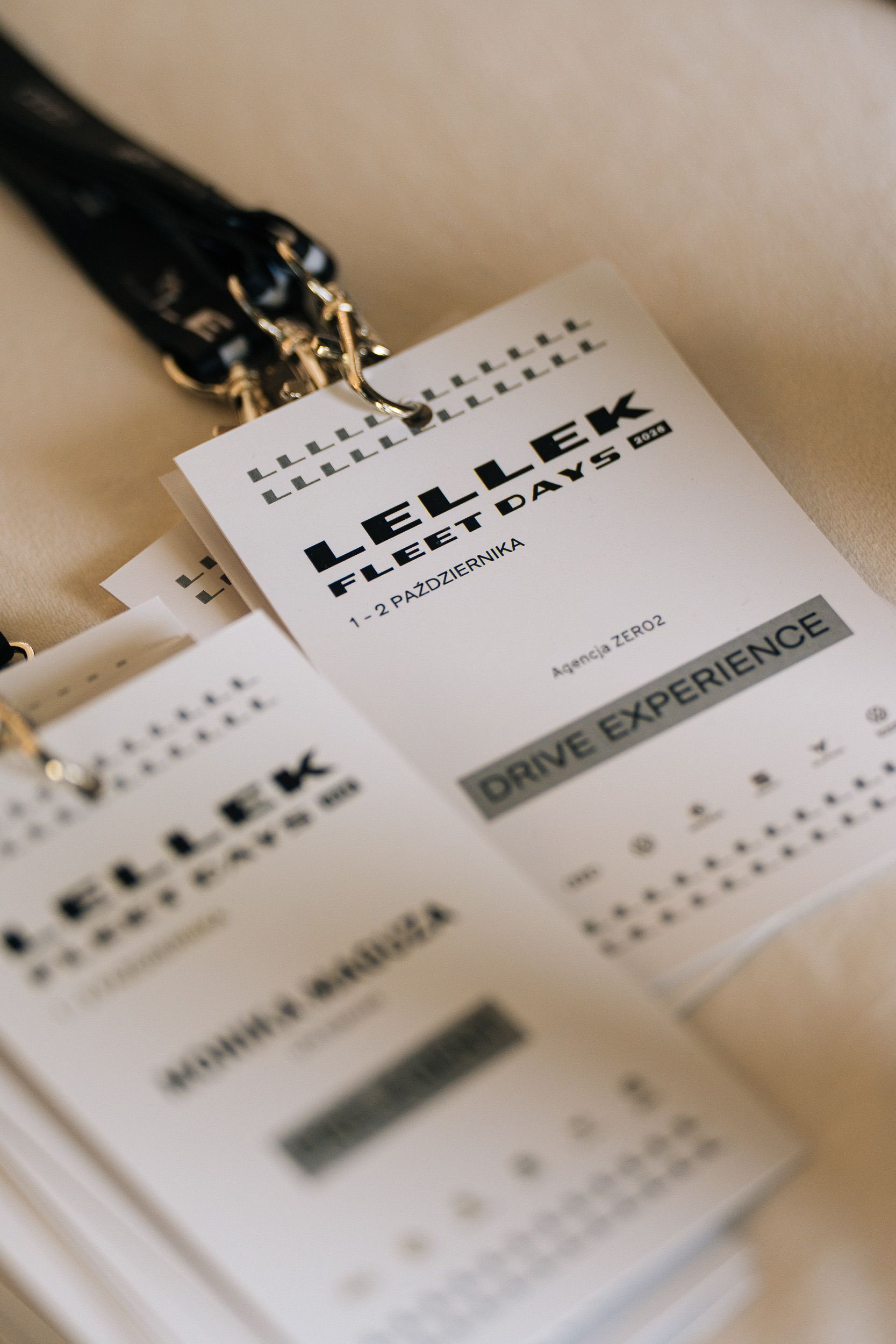 Identyfikatory na smyczach z logo LELLEK FLEET DAYS 2026 i napisem DRIVE EXPERIENCE na welcome desku